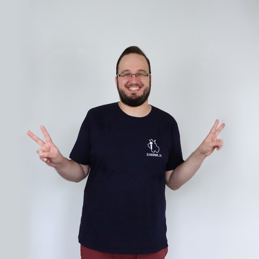 Ein Mann mit Brille und Bart lächelt und hält beide Hände zum Peace-Zeichen hoch, während er ein marineblaues T-Shirt mit dem kleinen Slam OWL-Logo aus der „T-Shirt Poetry Slam – Slam OWL – Logo & Eule“-Kollektion von Artbookings/Shirtigo trägt.