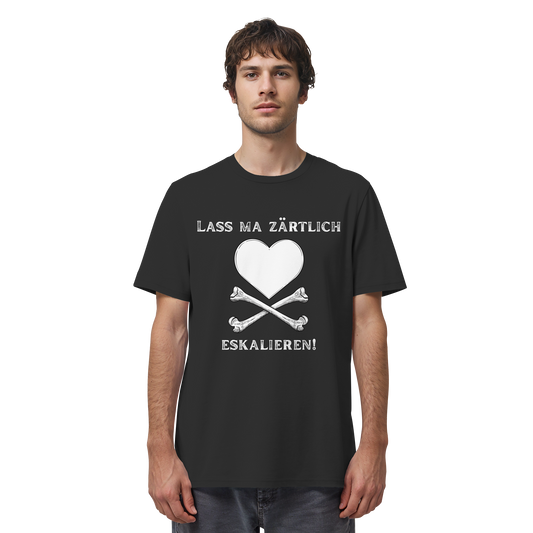 Ein Mann trägt das Artbookings/Shirtigo-Statement-T-Shirt „Lass ma zärtlich eskalieren!“ in Bio-Qualität mit einem schwarzen Motiv, das ein weißes Herz und gekreuzte Knochen zeigt – ideal für Fans von „Krawall + Zärtlichkeit“ oder dem Poetry Slam Essen.