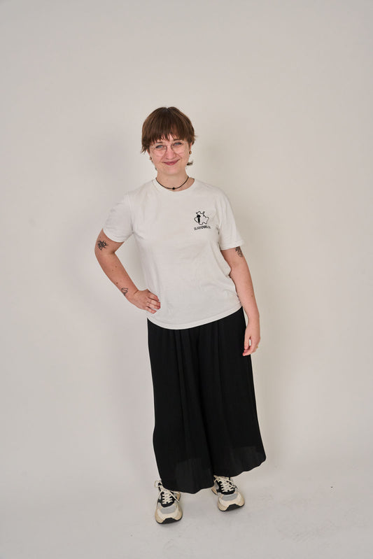 Mit dem "T-Shirt Poetry Slam - Slam OWL - Logo & Eule" von Artbookings/Shirtigo steht eine kurzhaarige, brillentragende Person in schwarzem Rock und Turnschuhen selbstbewusst vor dem nächsten Poetry Slam in Ostwestfalen-Lippe.