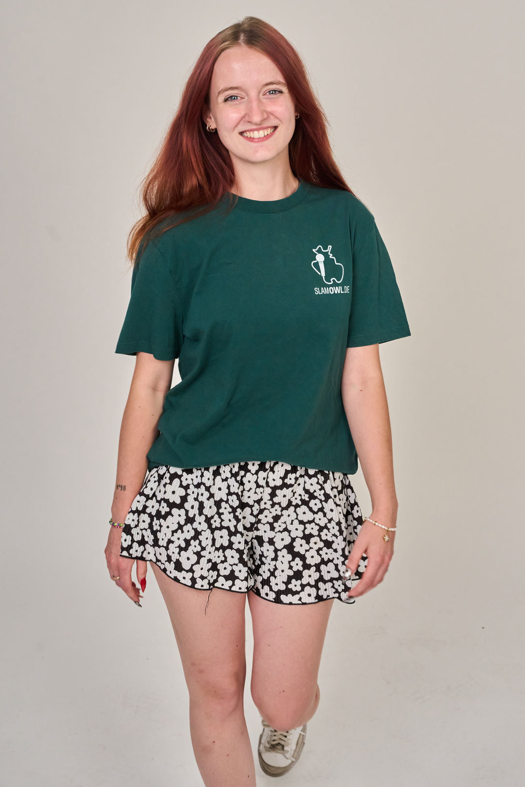 Eine junge Frau mit langen roten Haaren trägt das T-Shirt Poetry Slam - SLAM OWL - Logo & Eule - weiß auf Farbe | Bio-Qualität" von Artbookings/Shirtigo und verkörpert mit ihrem lässigen Selbstbewusstsein den lebendigen Geist der Poesie in Ostwestfalen-Lippe.