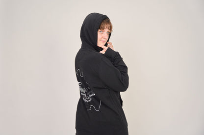 Eine Person posiert vor einem schlichten Hintergrund, trägt den Artbookings/Shirtigo Hoodie Poetry Slam - SLAM OWL in Bio-Qualität, mit weißem Eulen-Logoaufdruck auf dem Rücken, die Kapuze hochgezogen und schaut über die Schulter.