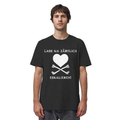 Ein Mann trägt das T-Shirt zum Krawall + Zärtlichkeit-Poetry-Slam „Lass ma zärtlich eskalieren!“ von Artbookings/Shirtigo mit einem schwarzen Motiv, das ein weißes Herz und gekreuzte Knochen sowie deutschen Text zeigt, hergestellt in Bio-Qualität – ideal für Fans des Poetry Slam Essen.