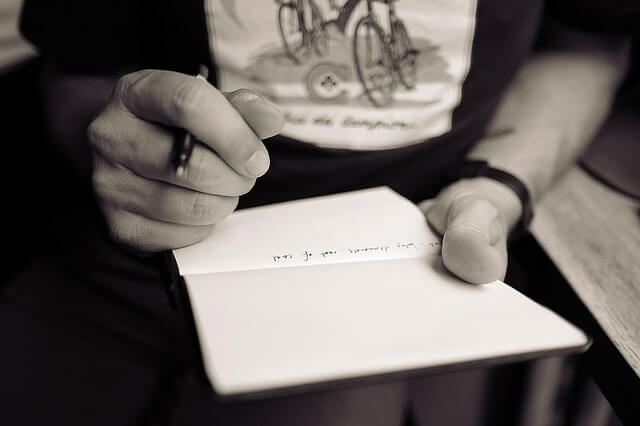 Ein Mann, der seine Gedanken kreativ mit einem Artbookings-Stift in ein Notizbuch schreibt, inspiriert von Kunstdrucken und Fotografie für potenzielle Poetry-Slam-Stücke.